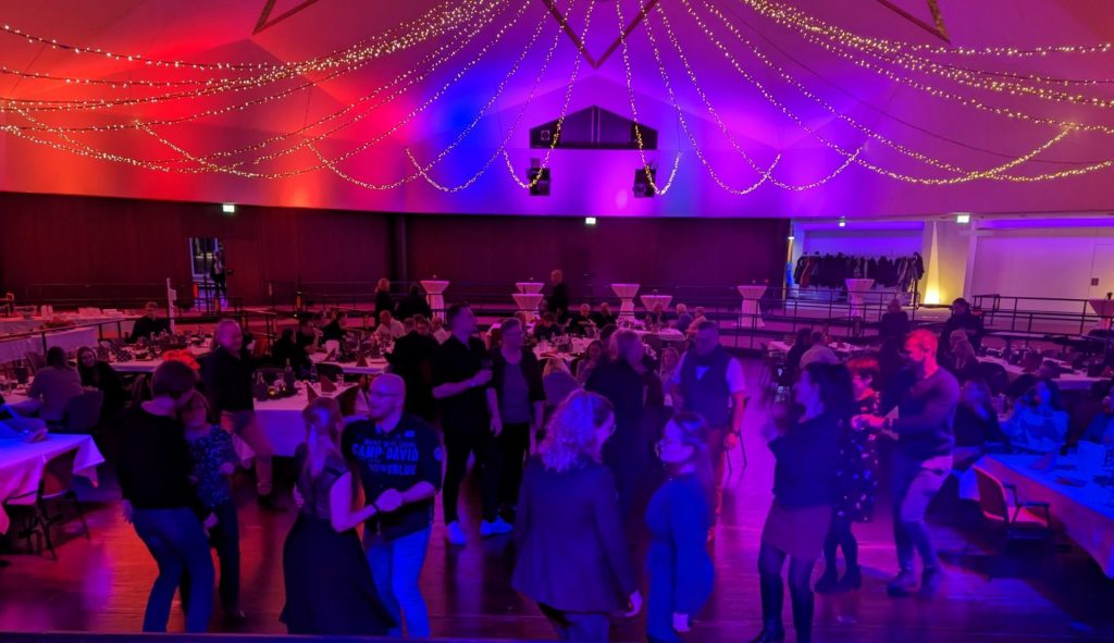 Viele Partygäste tanzen in einer großen, rot-blau beleuchteten Halle