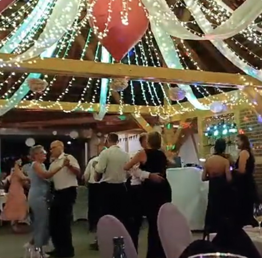 Paare tanzen unter Lichterketten und Dekoration in einer Scheune